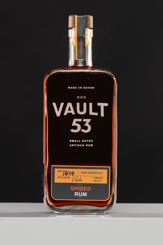 A bottle of Vault 53 Spiced Rum with a dark label and orange text, indicating the flavor profile of orange and pineapple.