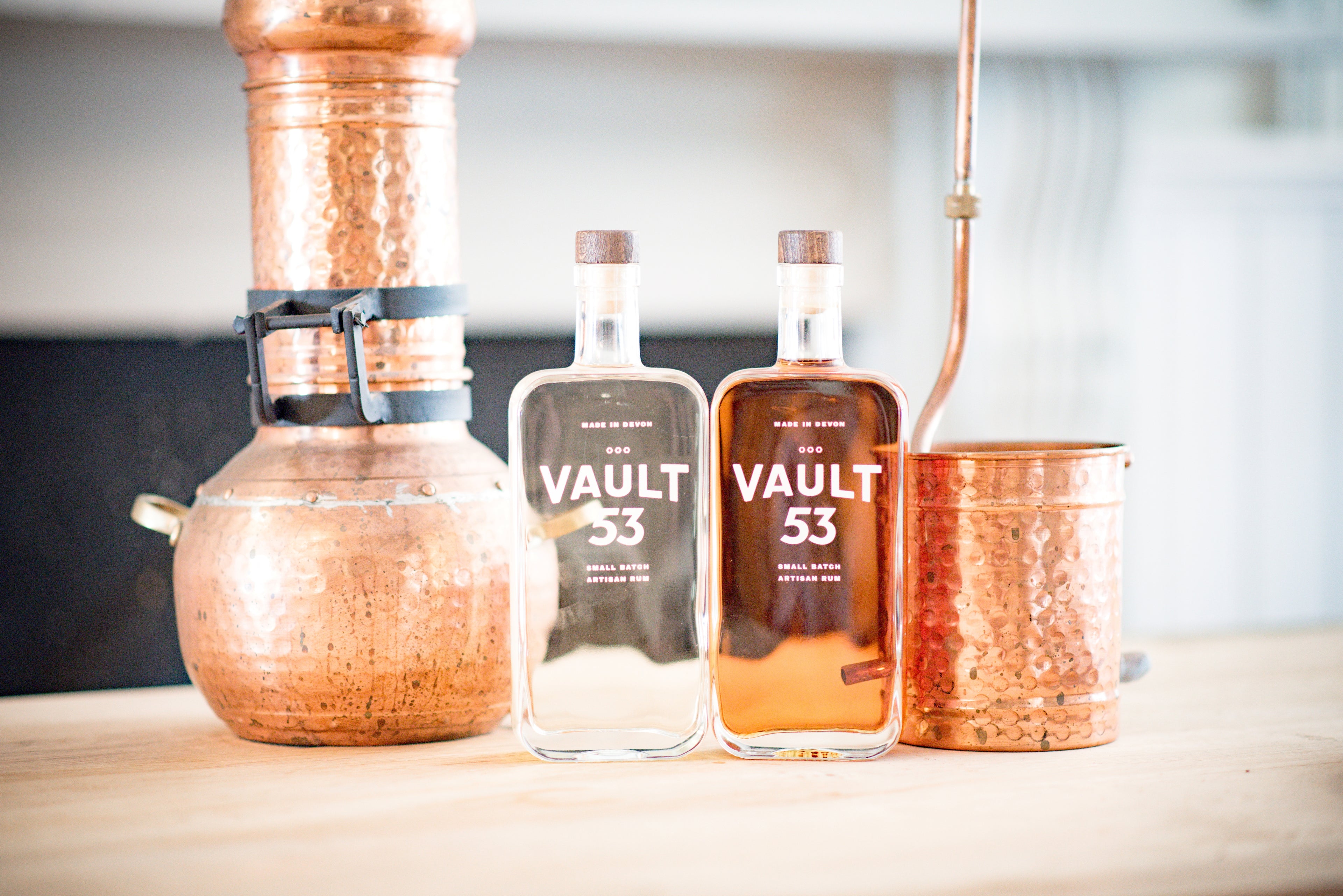 A picture of two bottles of rum sat in between a small pot still.