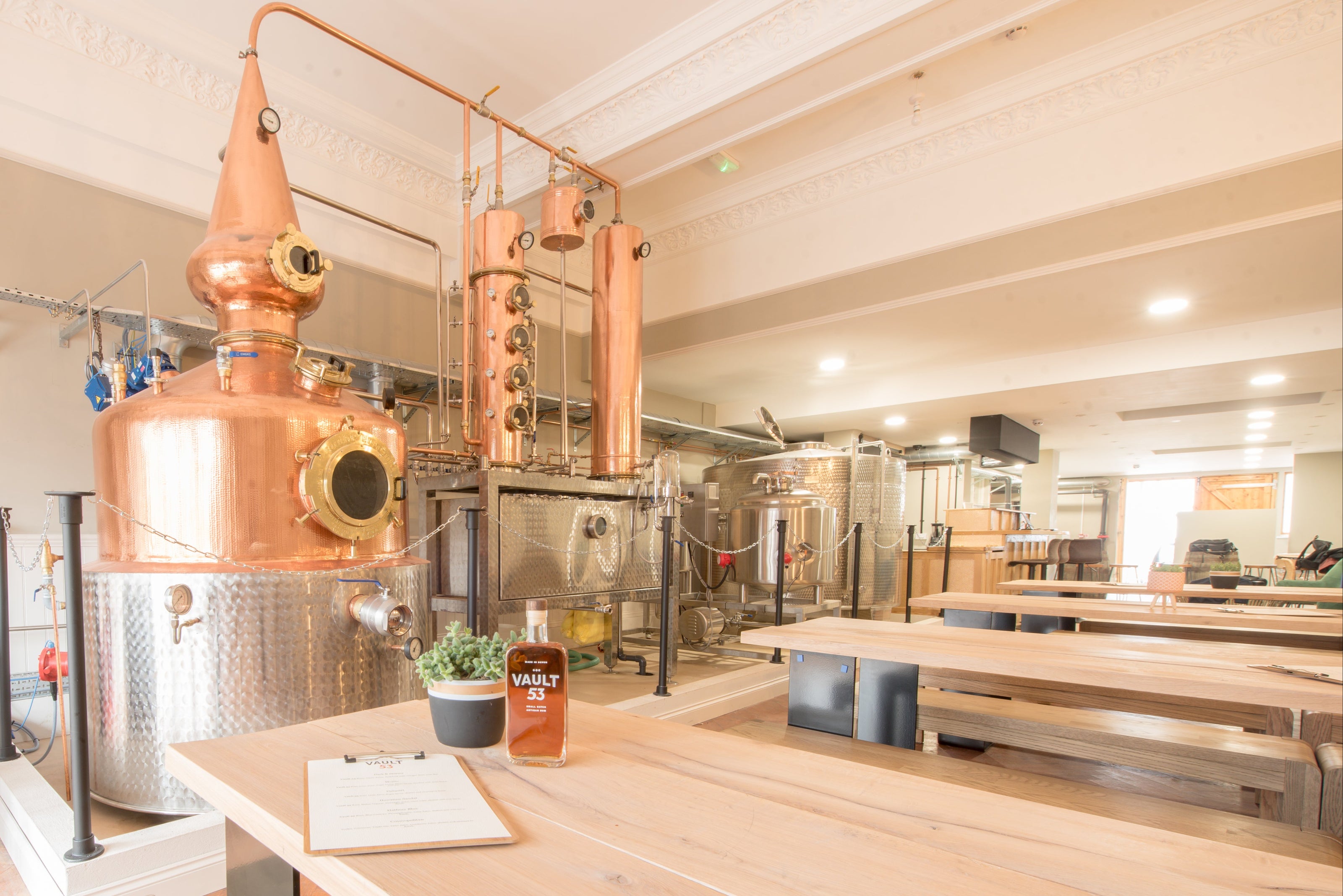 Copper distillation tanks in a modern brewery with wooden tables and stools.