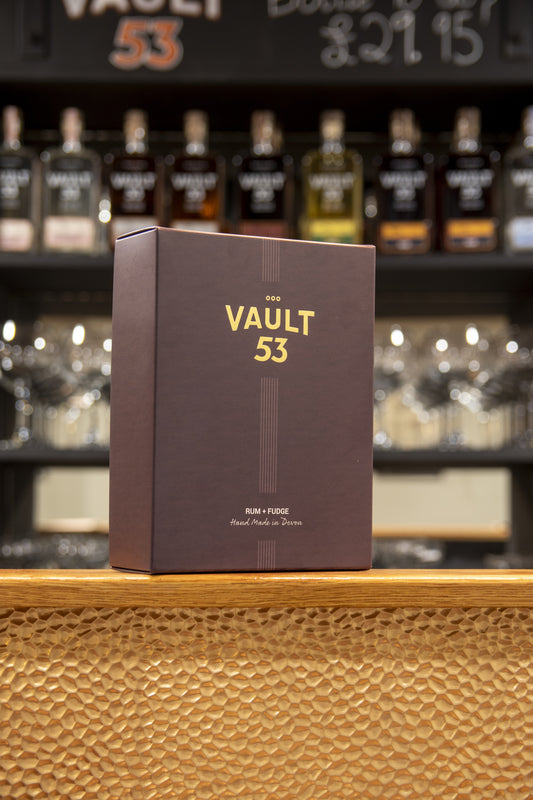 Brown box labeled 'The Vault 53' on a wooden surface with blurred bottles in the background
