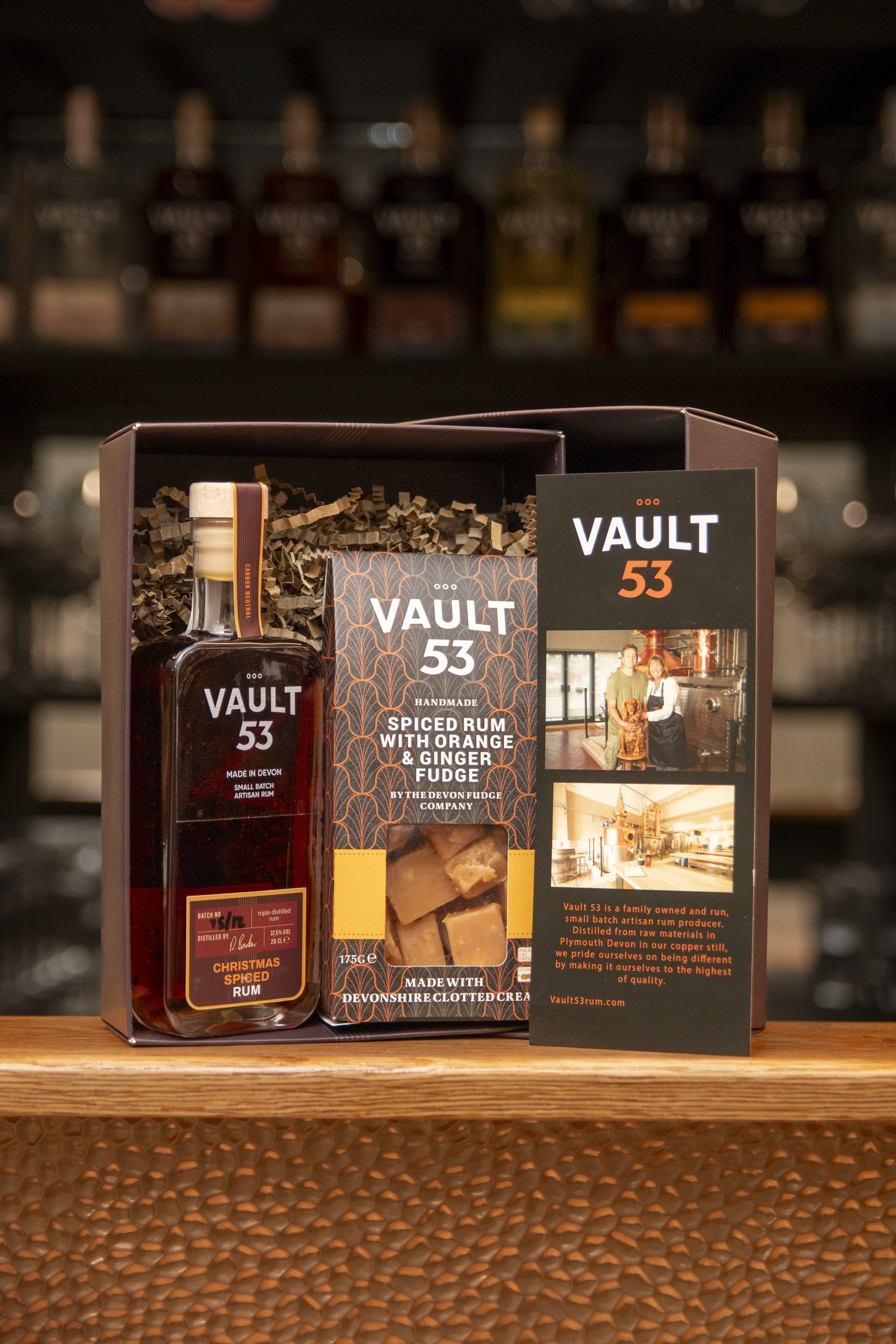 Vault 53 spiced rum bottle and packaging on a wooden surface with blurred bottles in the background